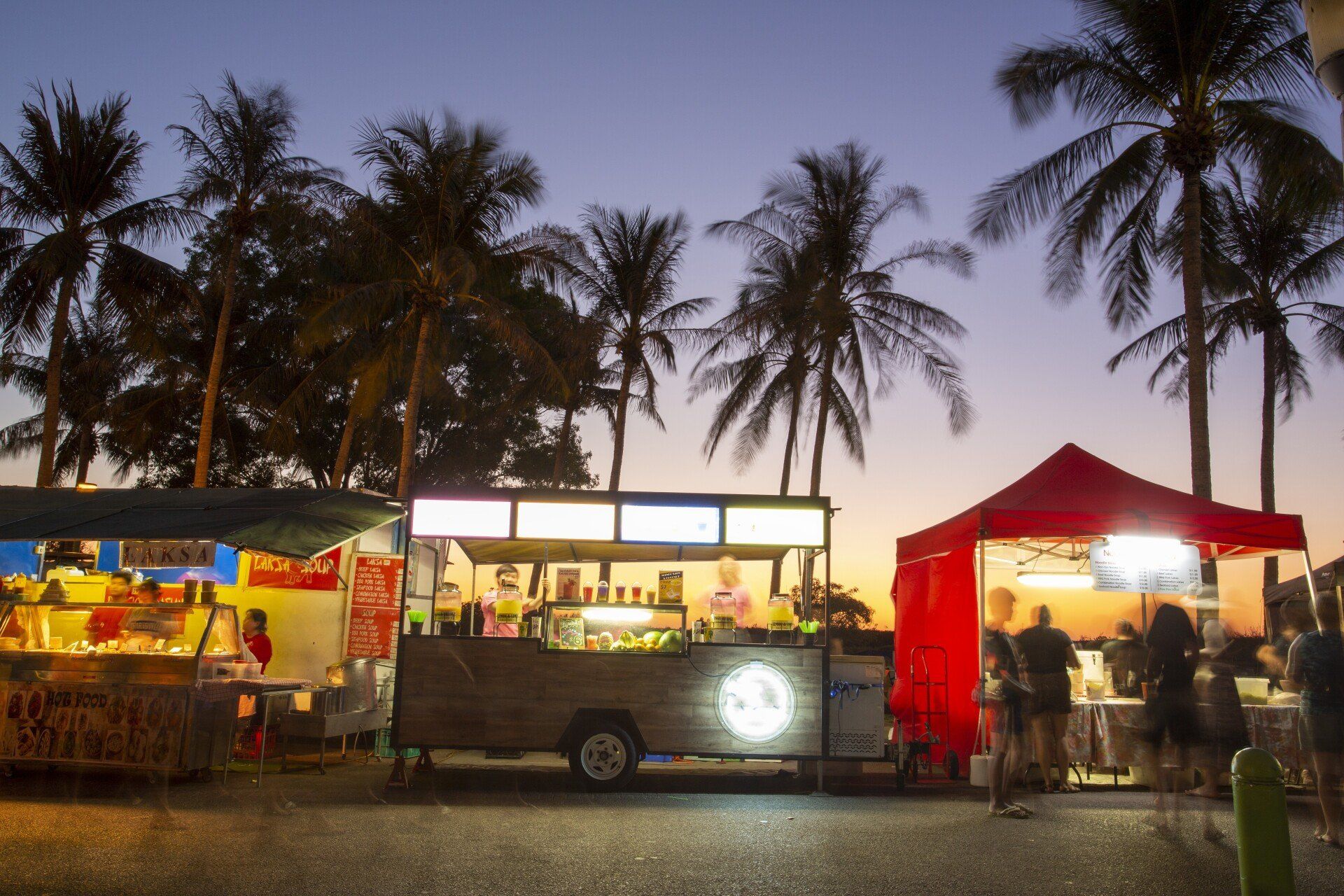 A row of food trucks are parked in front of palm trees