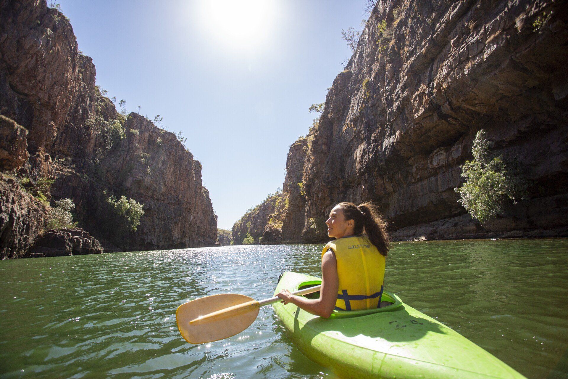 A woman is paddling a green kayak down a river.