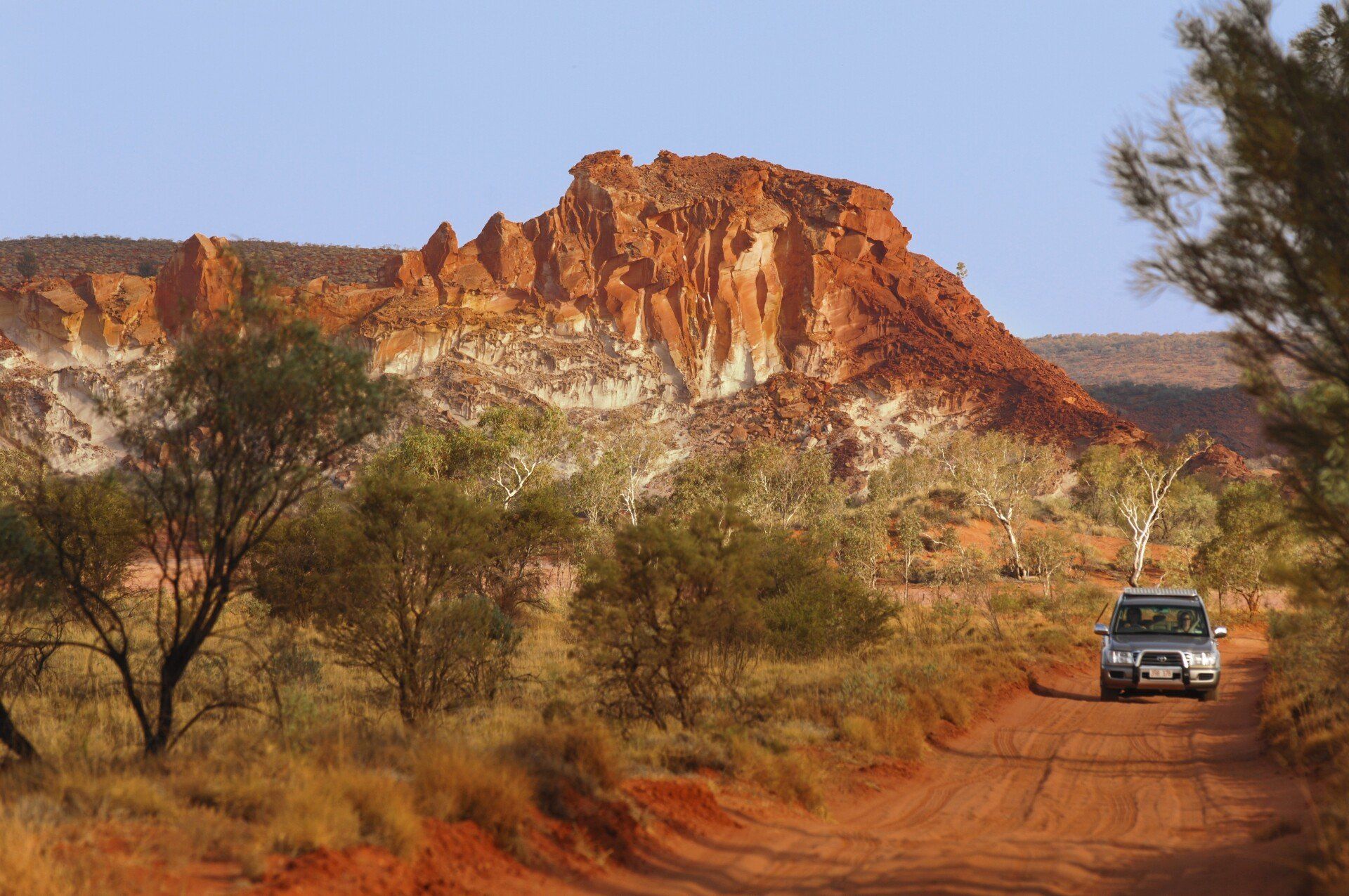 A car is driving down a dirt road in the desert.