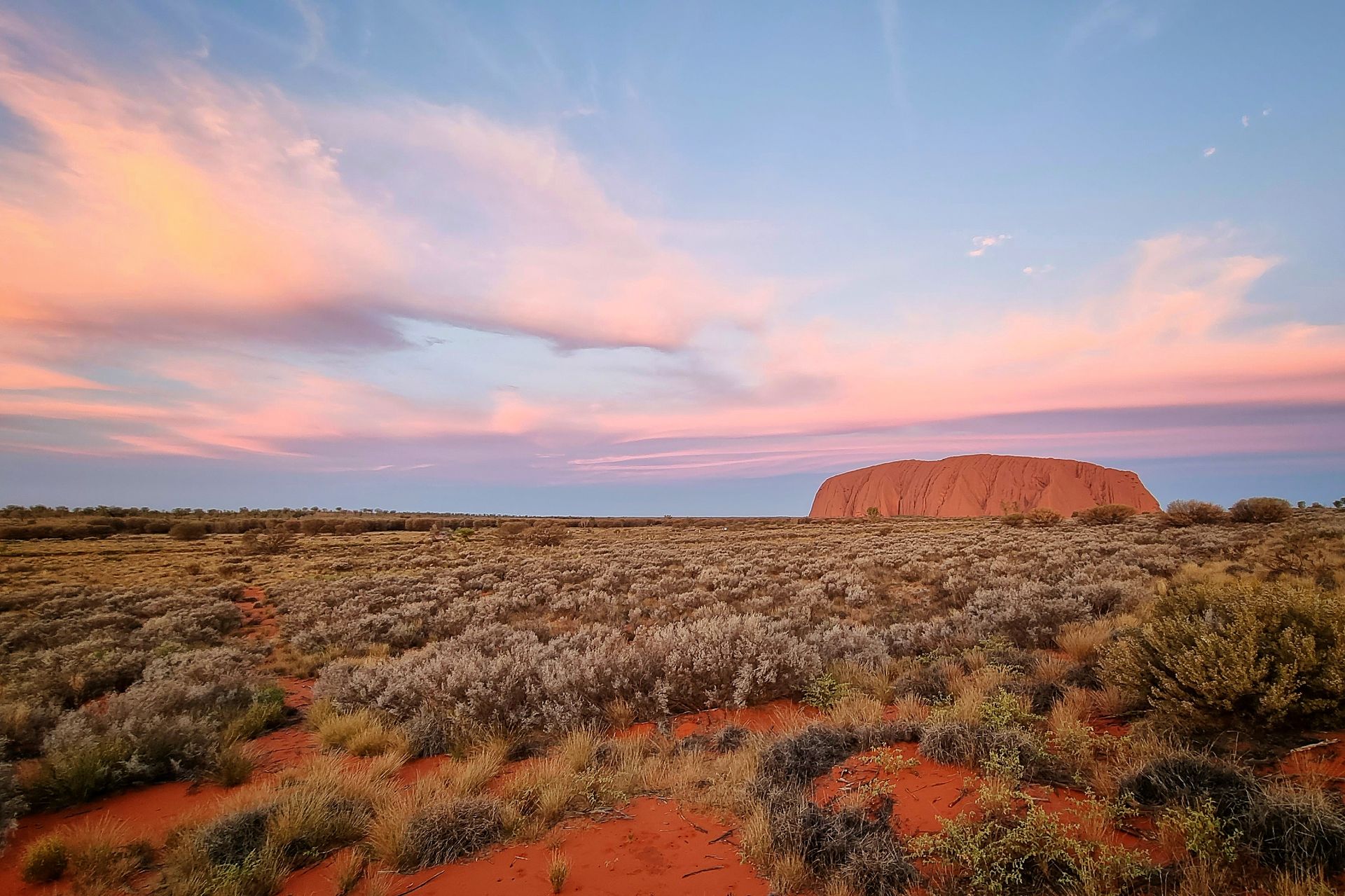 A desert landscape with a mountain in the background at sunset.