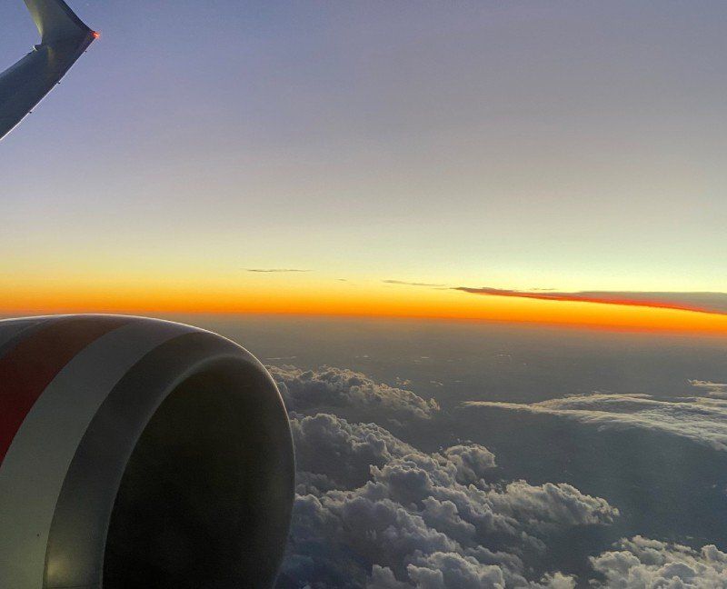 A plane is flying over a cloudy sky at sunset