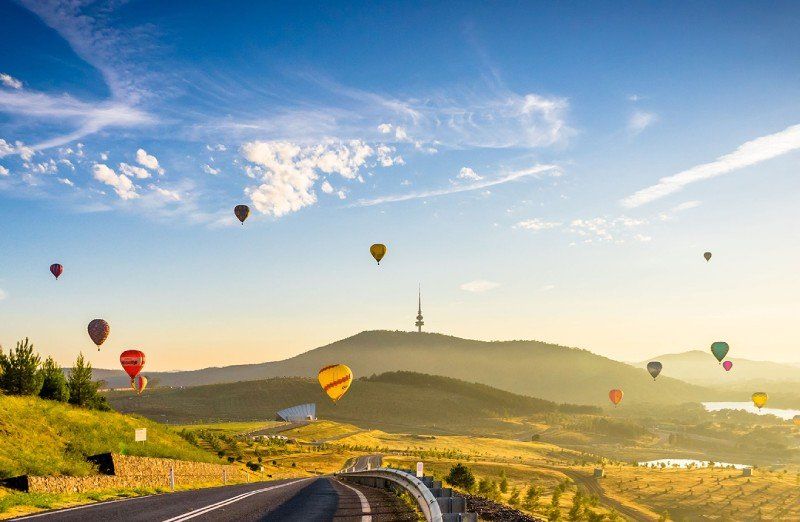 A bunch of hot air balloons are flying over a road.