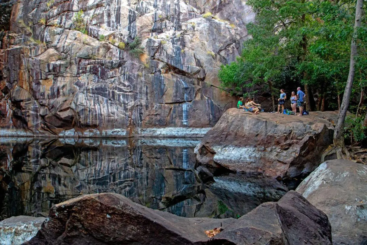 A group of people standing on top of a rock next to a body of water.