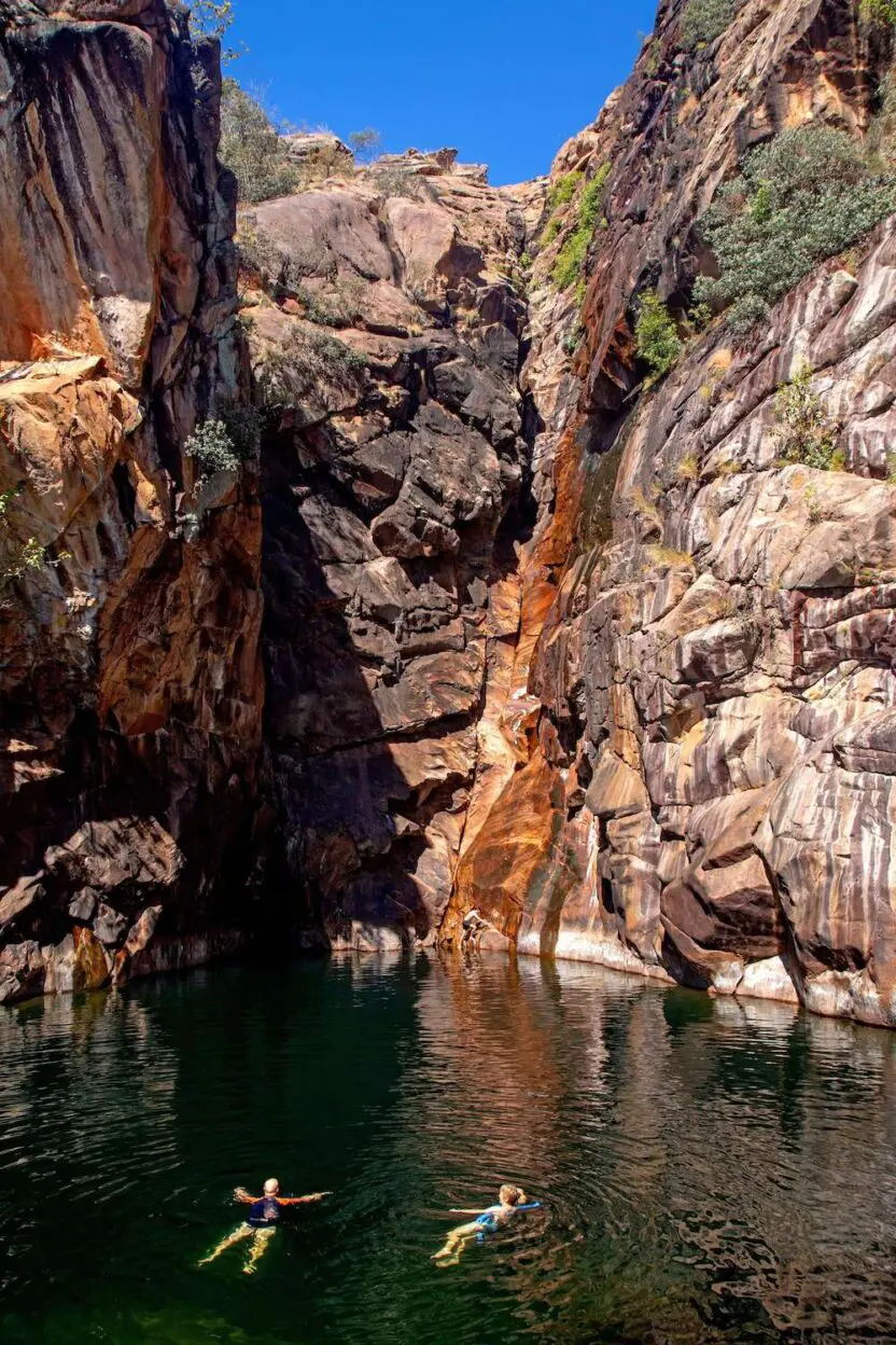 Two people are swimming in a river surrounded by rocks.
