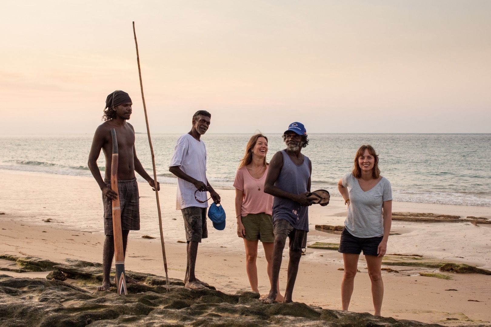 A group of people are standing on a beach next to the ocean.