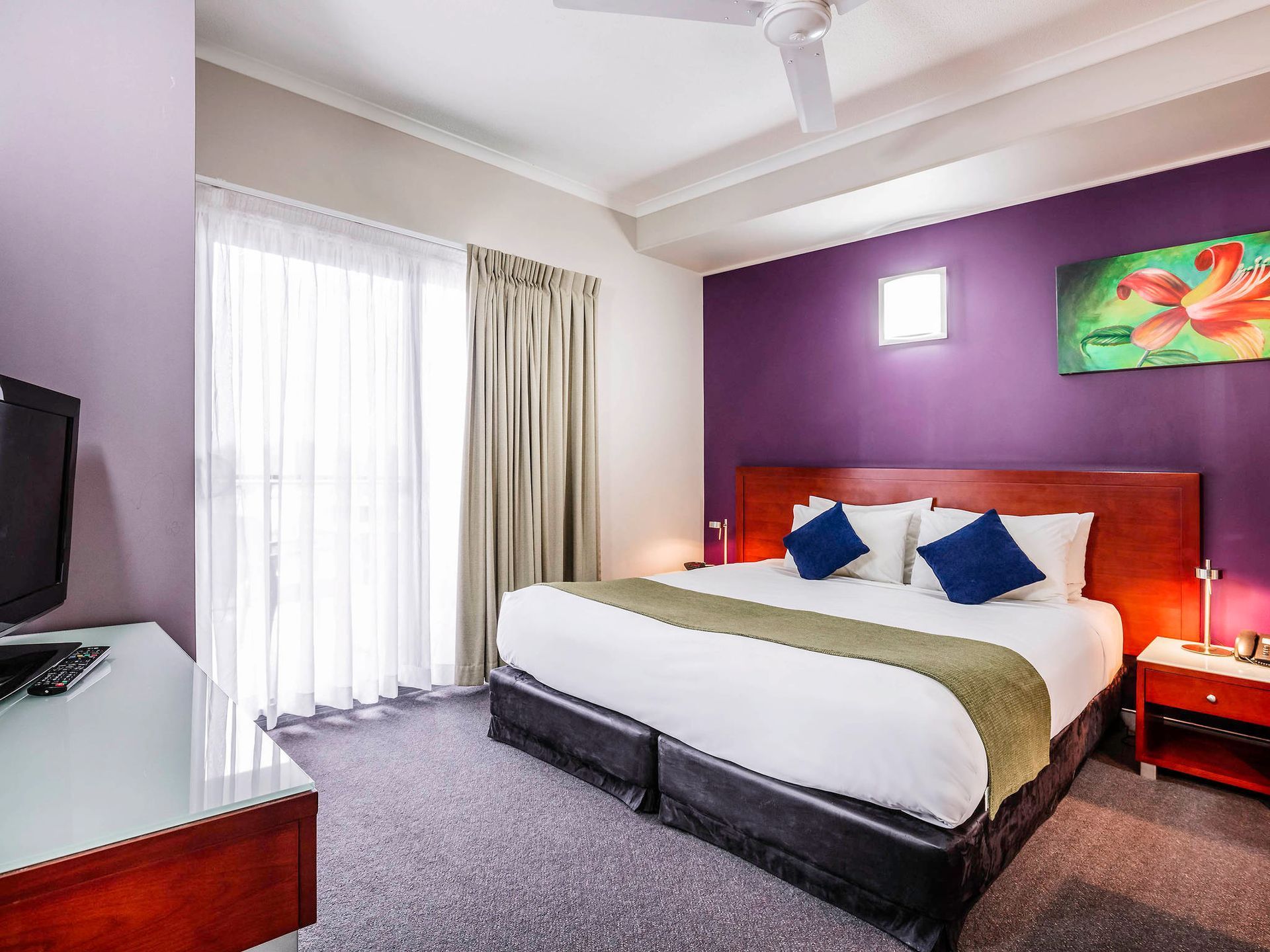 A hotel room with a king size bed , television , nightstand and purple walls.