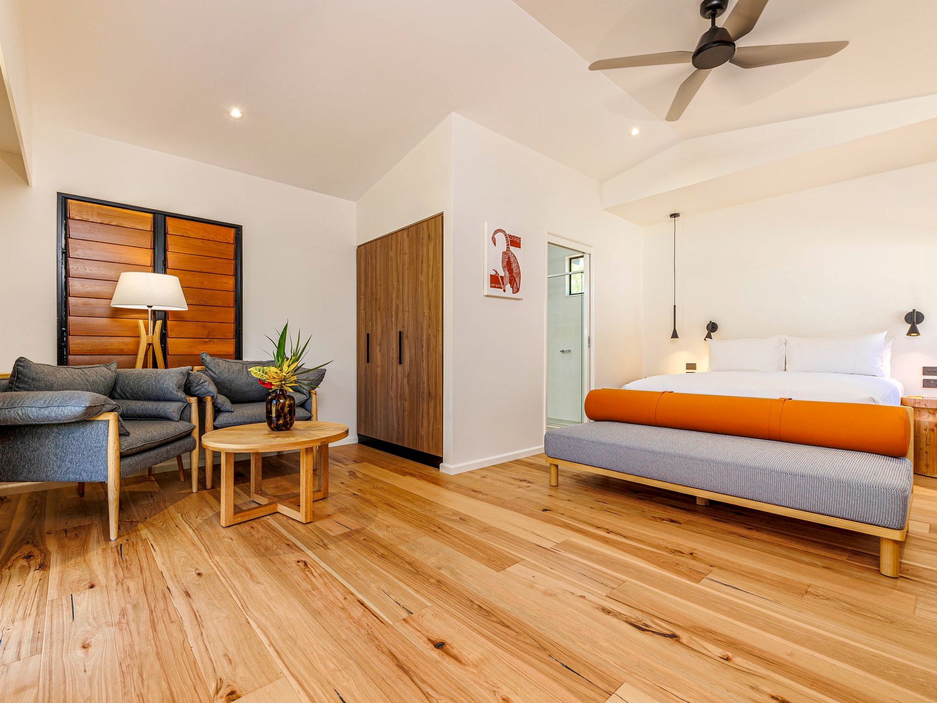 A hotel room with a king size bed , chairs , and a ceiling fan.