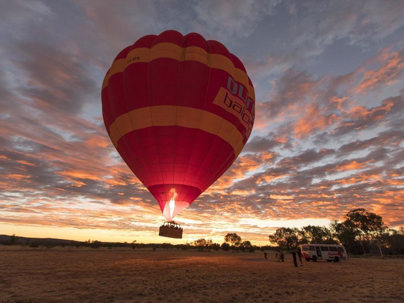 A hot air balloon is flying over a field at sunset.