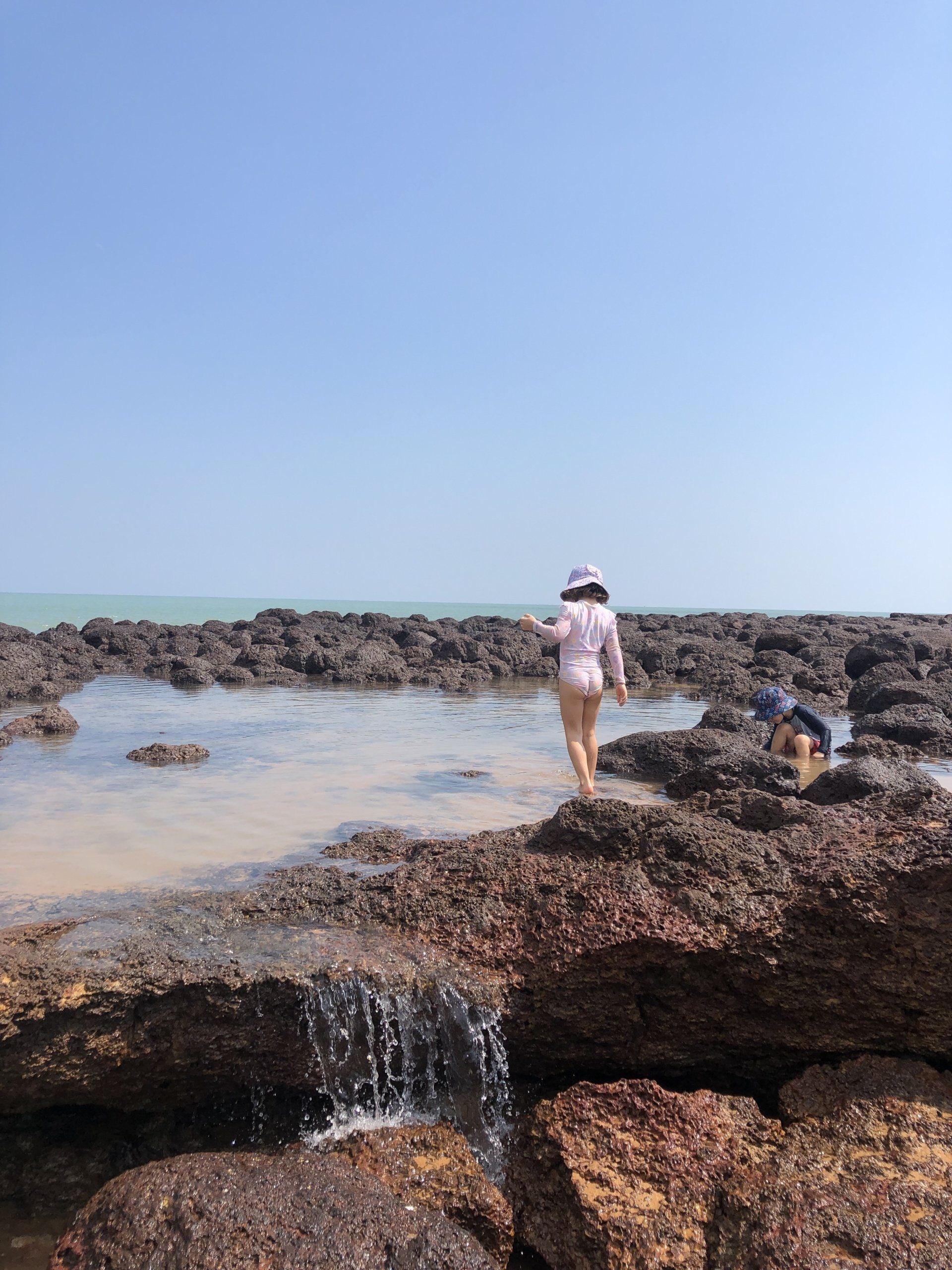 A woman is walking on a rocky beach near the ocean.