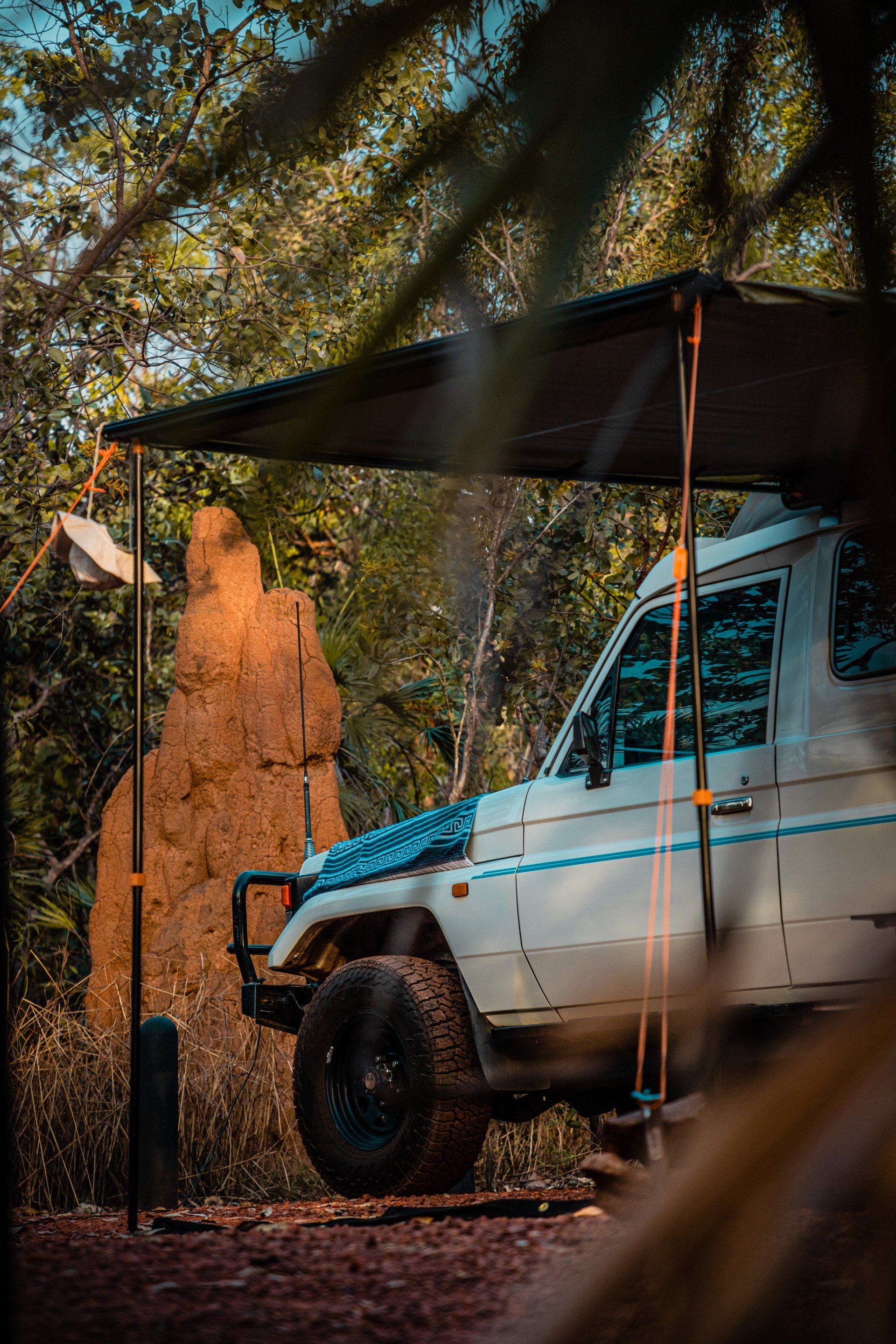 A white truck is parked under a canopy in the woods.