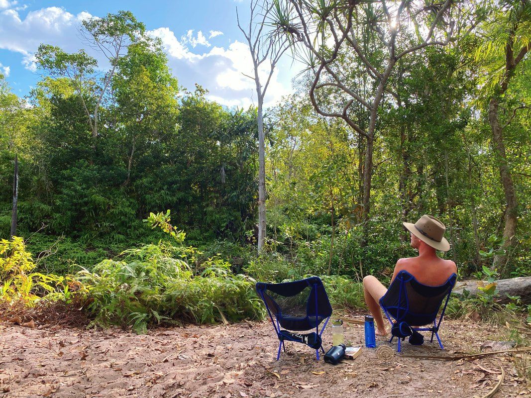 A man is sitting in a chair in the woods.