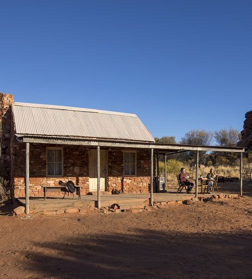 A brick house with a porch in the middle of a desert.