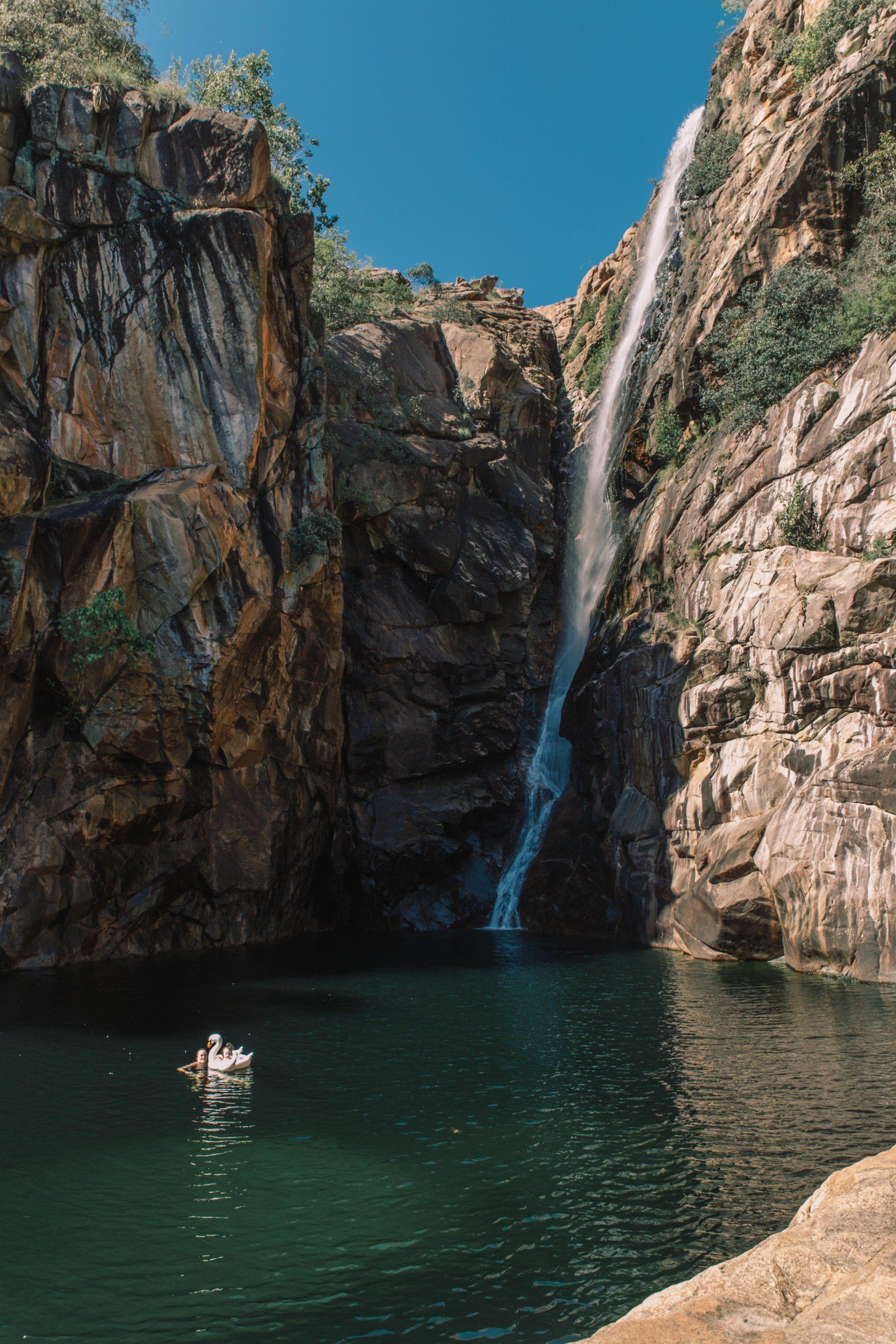 A waterfall in the middle of a canyon with a boat in the water.