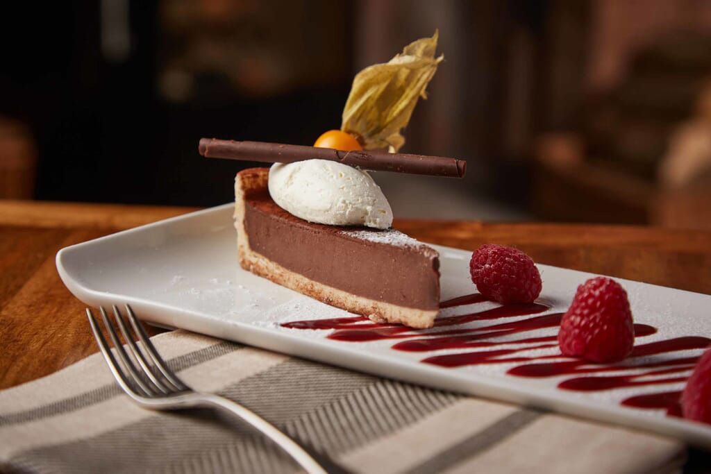 a slice of chocolate pie with raspberries and whipped cream on a plate with a fork .