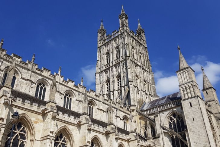 Gloucester Cathedral rises against a bright blue sky, showcasing its ornate, light-colored stone architecture.