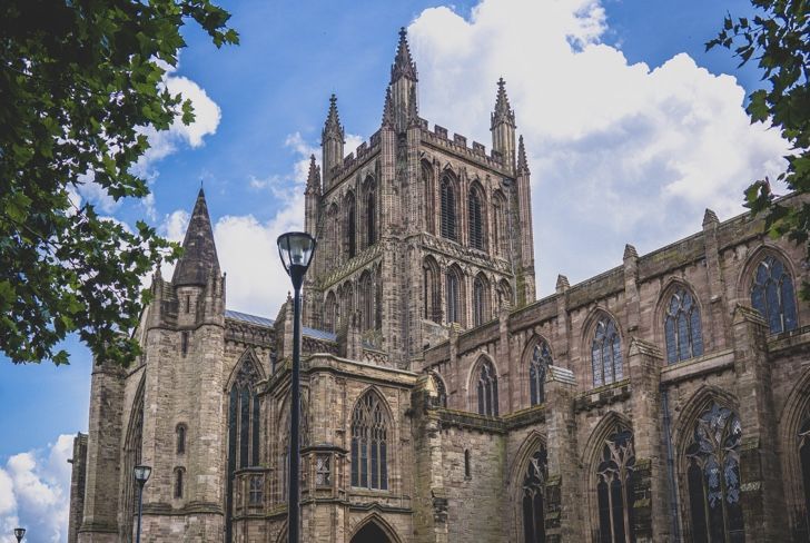 Hereford Cathedral, a large stone building with pointed arches and spires, under a blue sky with scattered clouds.