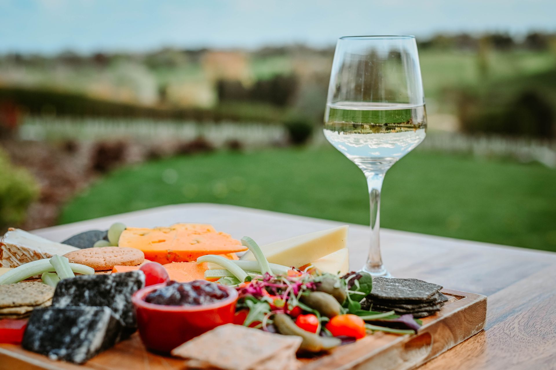A cutting board with cheese and a glass of wine on a table.