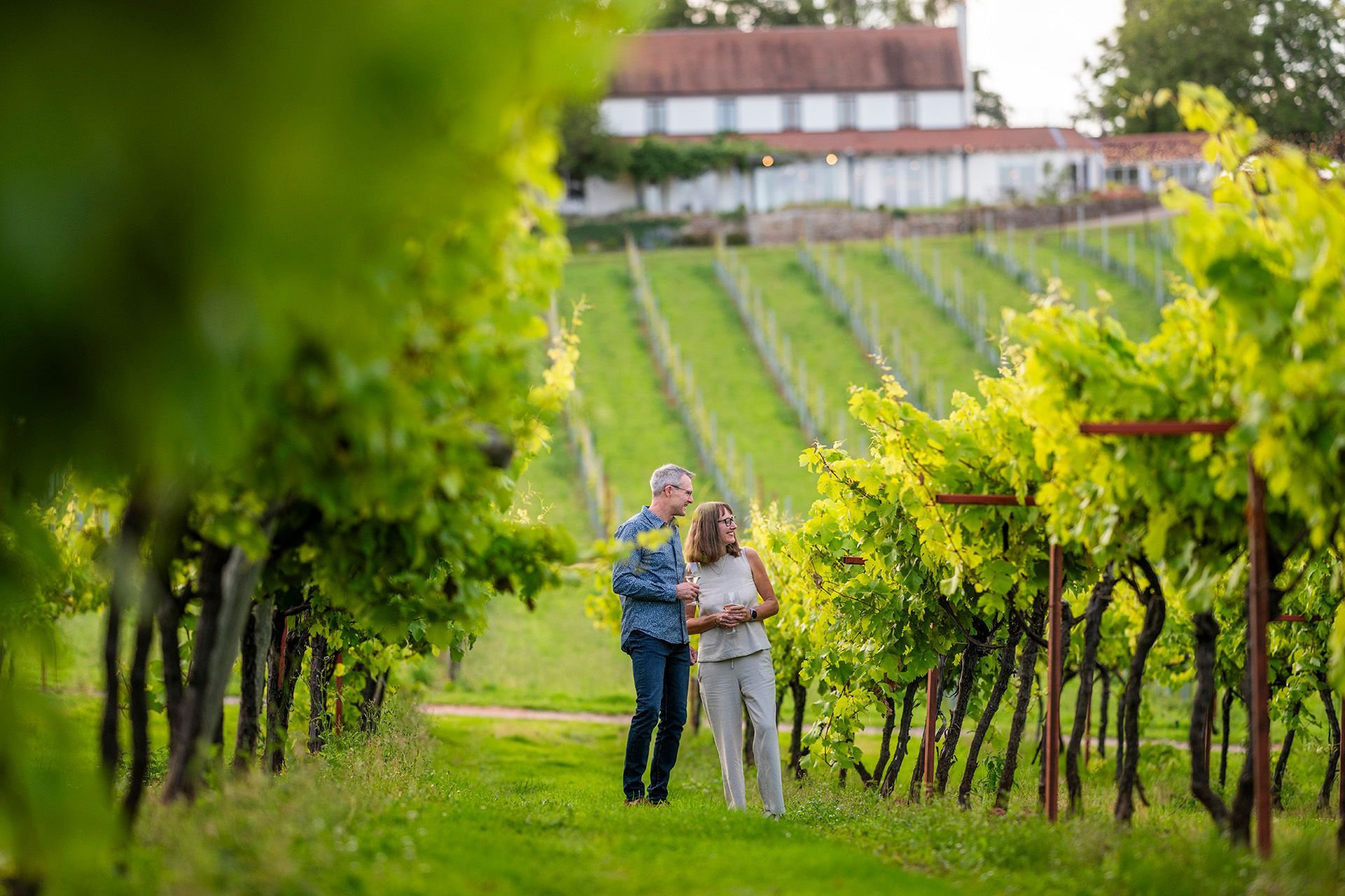 a man and a woman are standing in a vineyard .