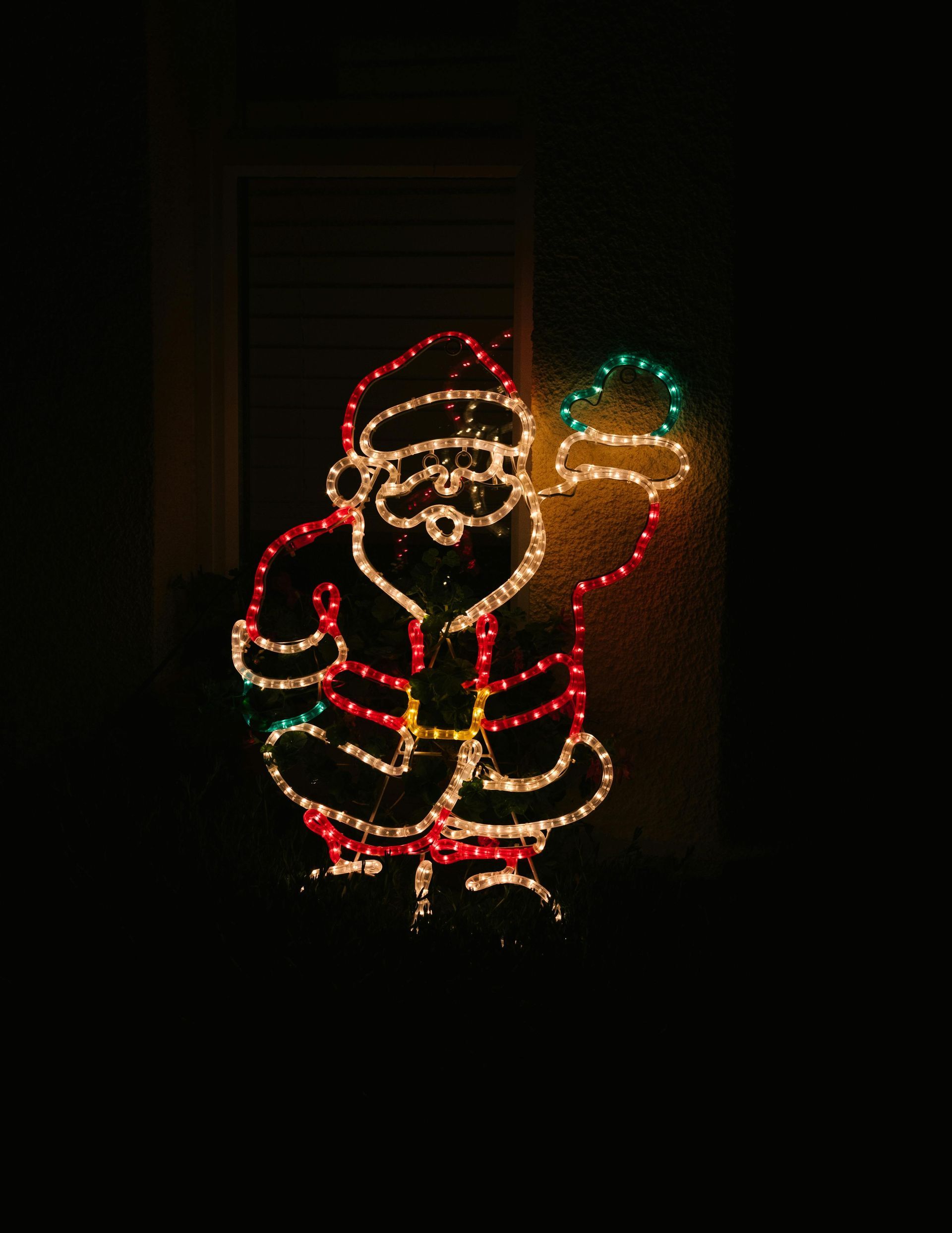 Santa Claus Christmas light display, holding a hat, lit up against a dark background.