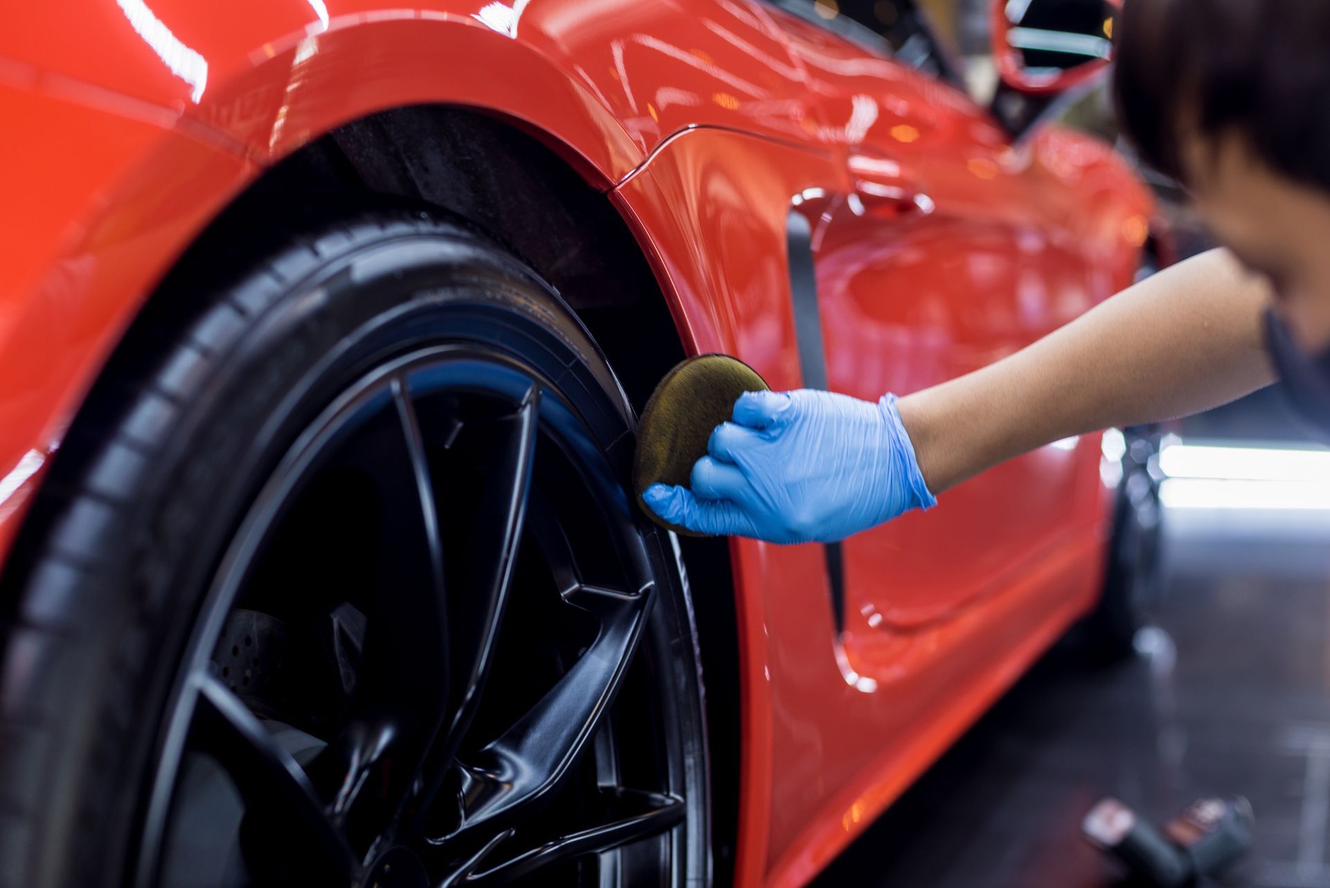 A person is polishing a red car with a sponge.