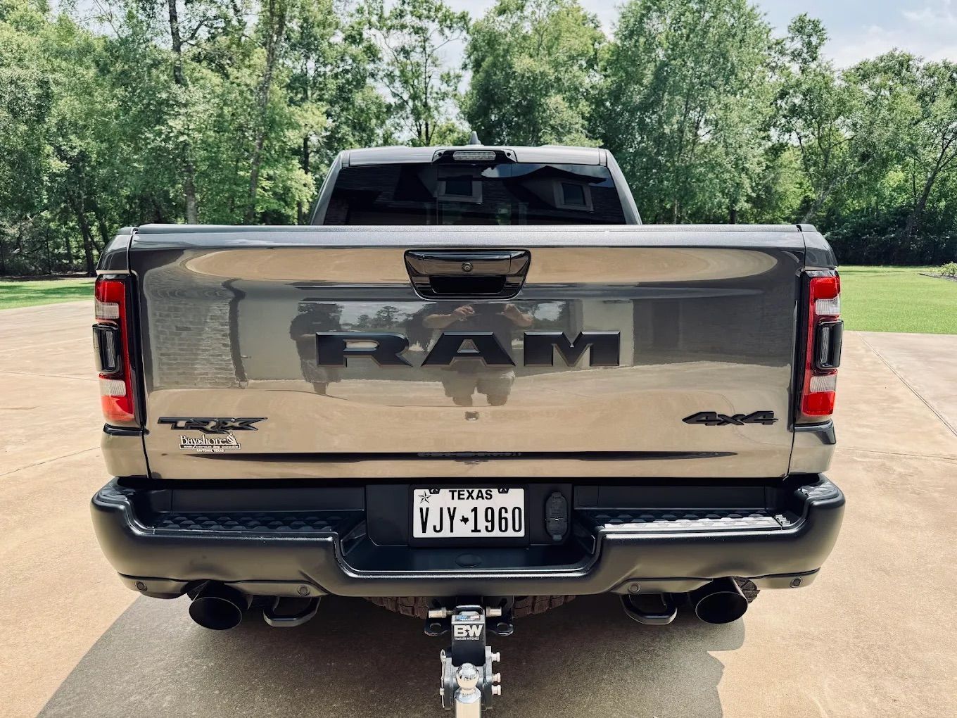 Back view of a bronze RAM 1500 truck with black badging, a black bumper, dual exhaust, and a Texas license plate.