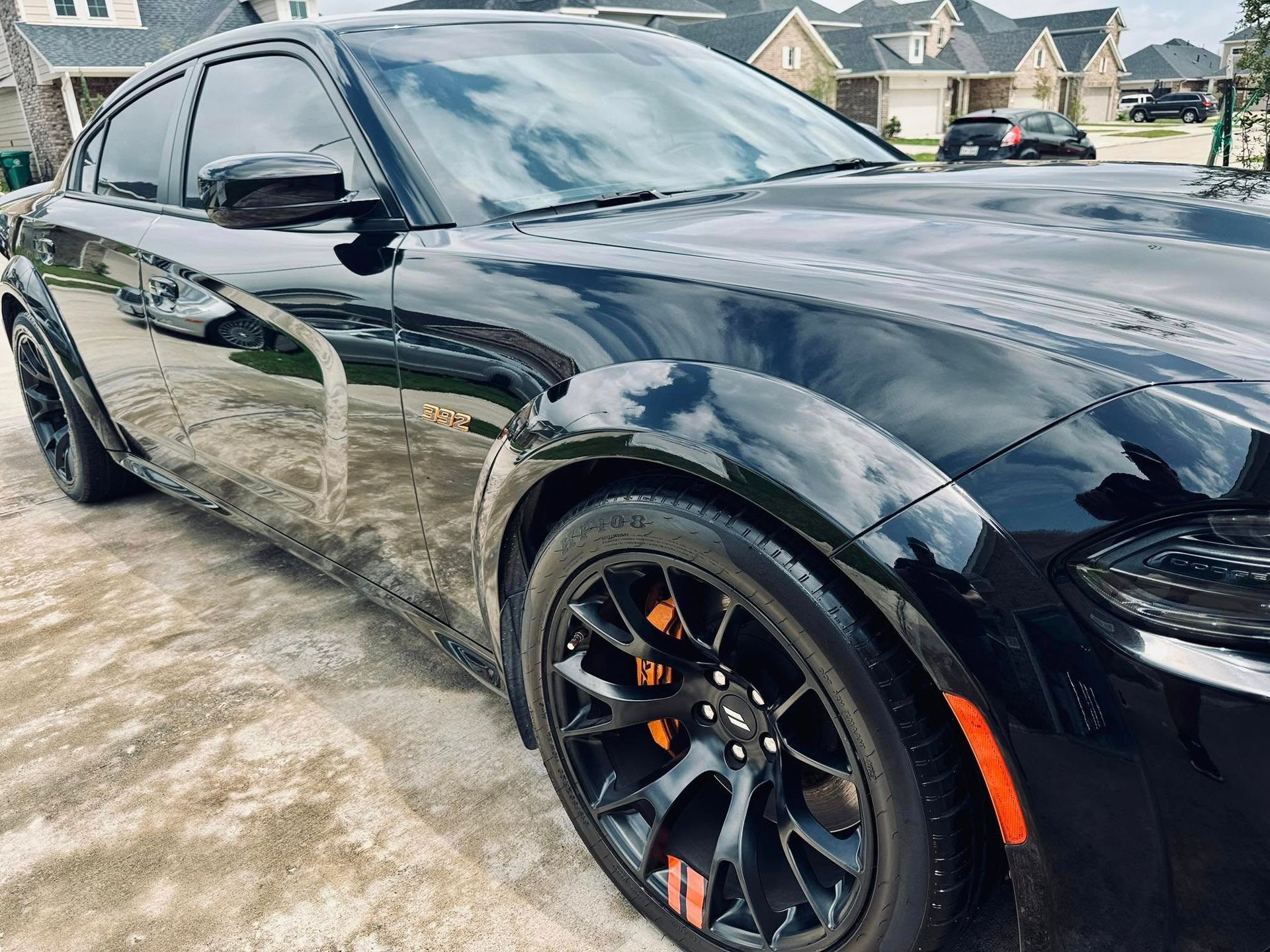 A sleek, glossy black sedan with wide-body fender flares and orange brake calipers parked on a residential driveway.