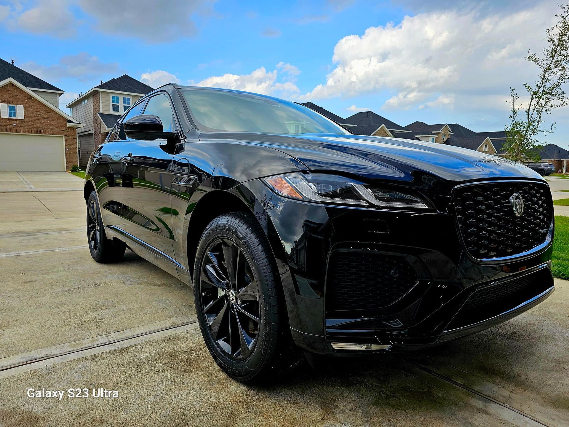 A black Jaguar SUV parked on a residential concrete driveway on a sunny day.