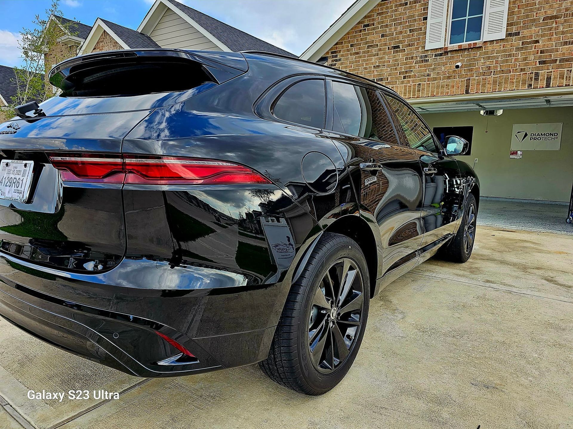 A black Jaguar F-Pace SUV parked on a paved driveway in front of a brick house.
