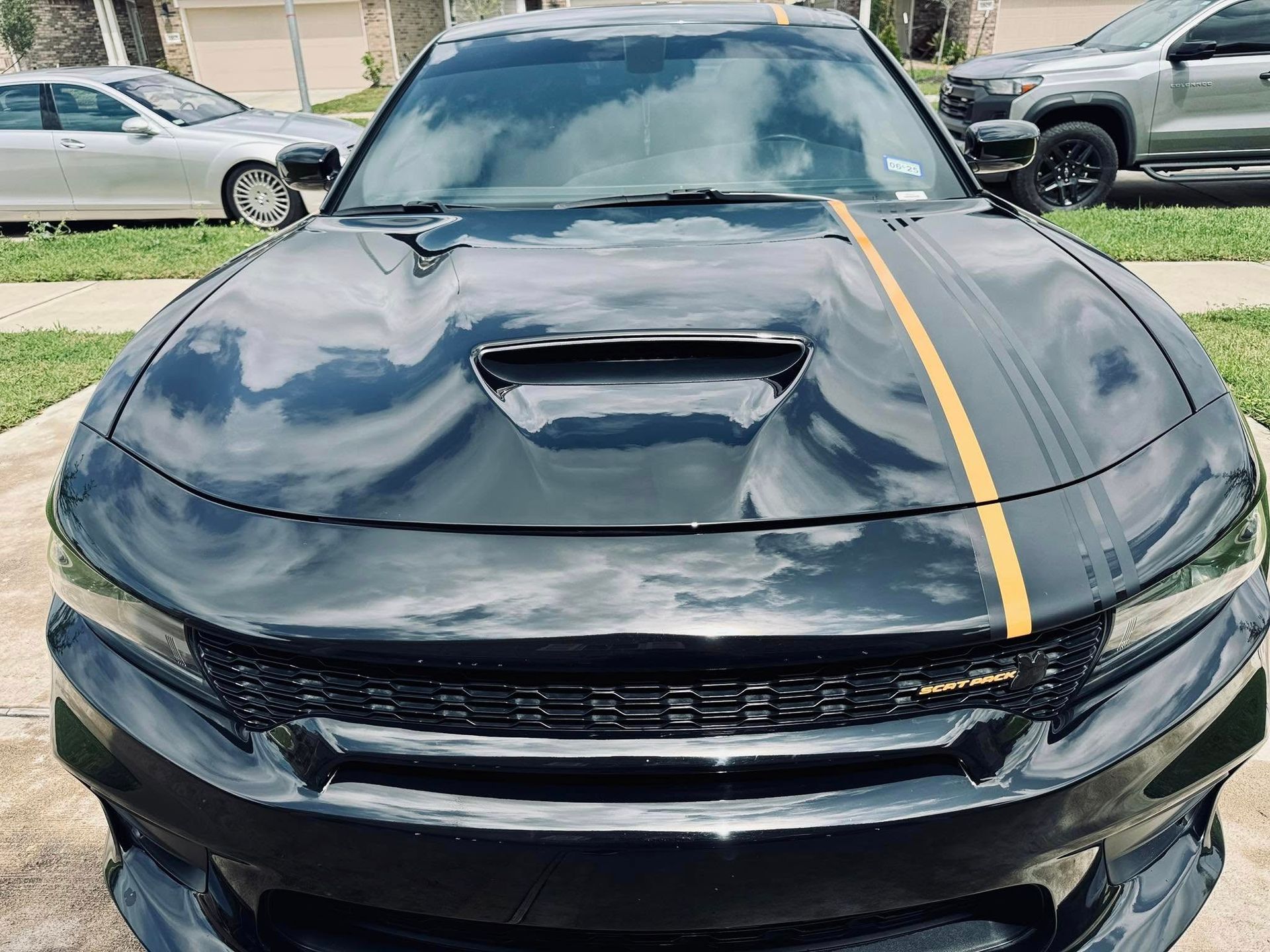 Black Dodge Charger with a hood scoop and single orange racing stripe, parked outdoors on a paved surface.