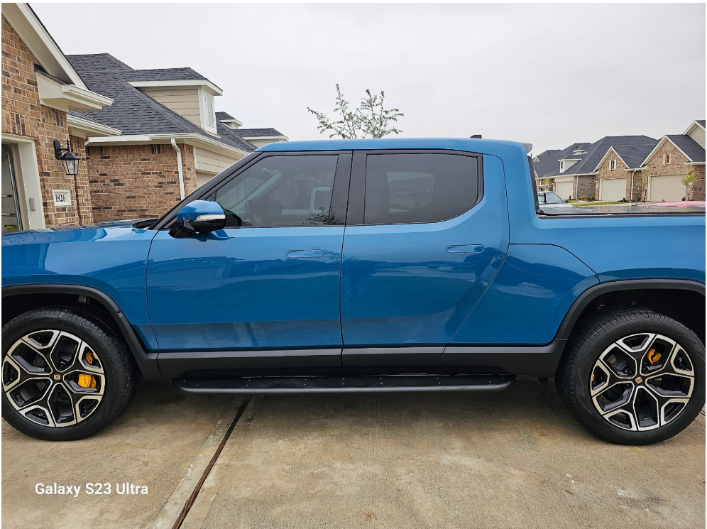 A blue electric pickup truck parked in a residential driveway on a cloudy day.