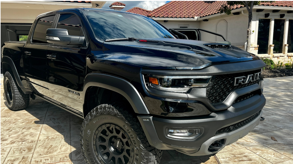 A black Ram TRX pickup truck parked on a patterned driveway in front of a house.