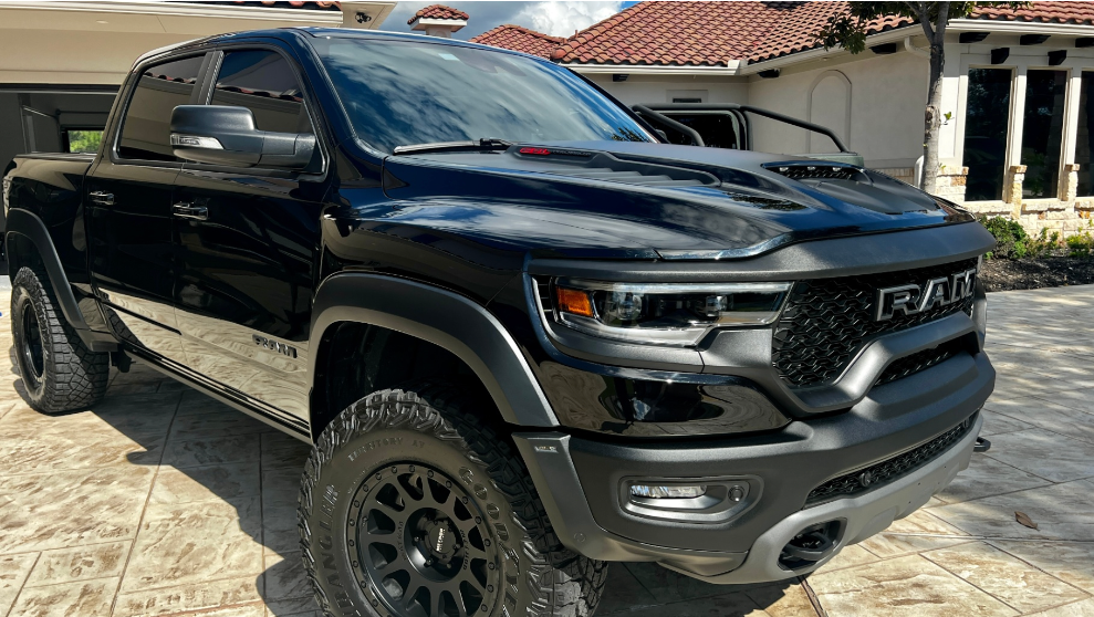 A black Ram TRX pickup truck parked on a patterned driveway in front of a stucco building.