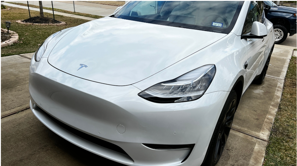 A white Tesla Model Y parked on a residential concrete driveway.