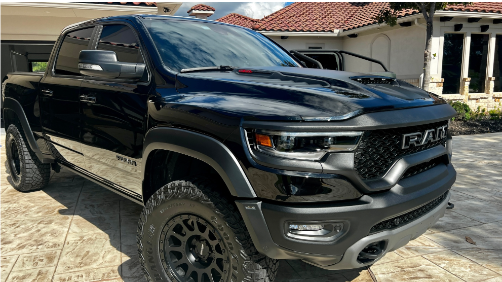 A black RAM TRX pickup truck parked on a patterned stone driveway in front of a house.