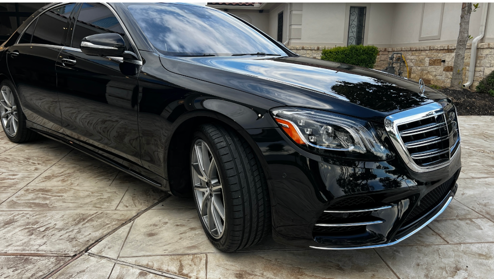 A shiny, black Mercedes-Benz S-Class sedan parked on a stone driveway.