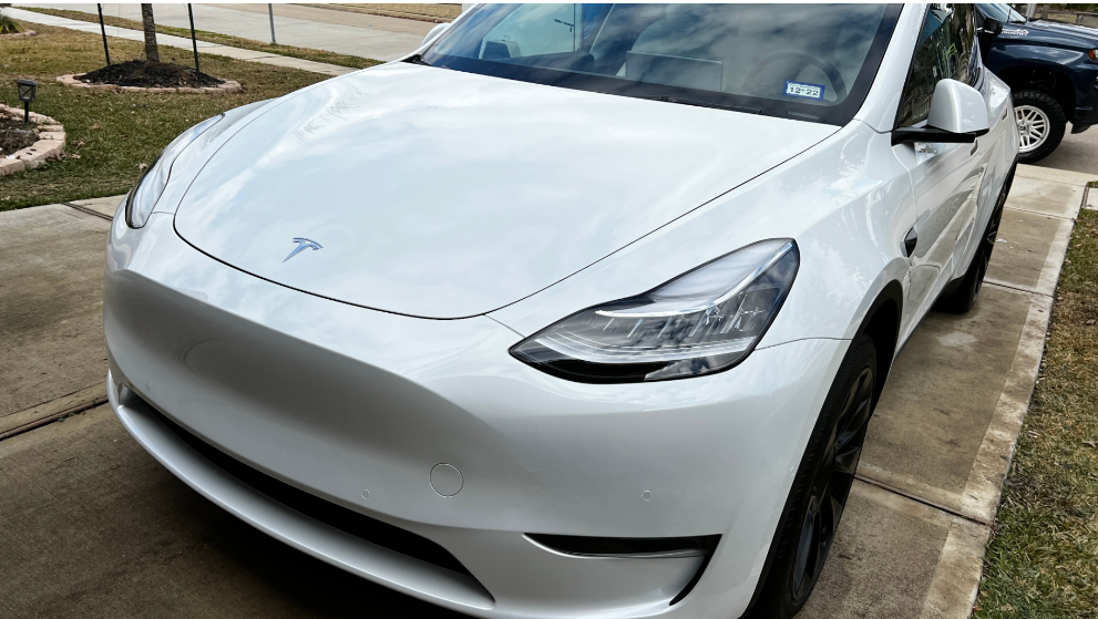 A white Tesla Model Y parked on a residential concrete driveway.