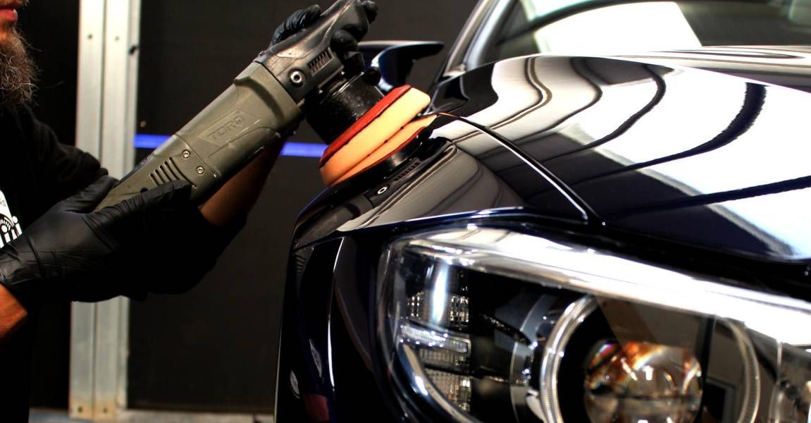 A man is polishing the hood of a car with a machine.