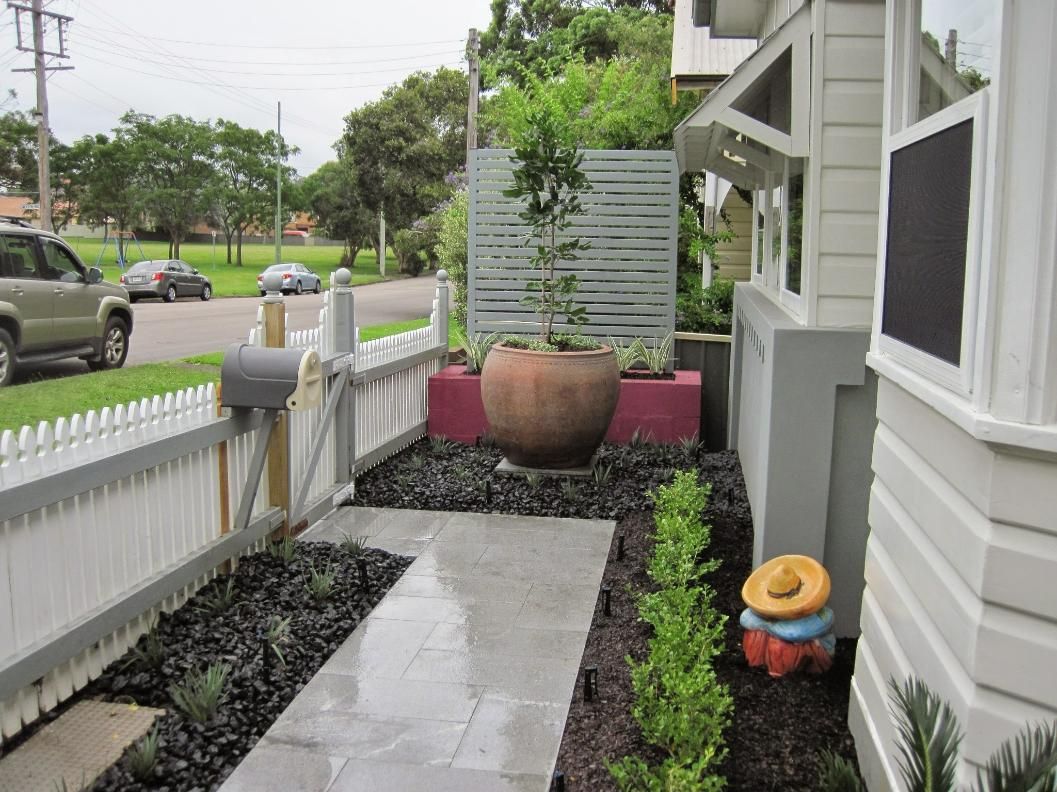 A Narrow Walkway With a White Picket Fence, With a Decorative Pot and a Colorful Stack — Green Envy Landscape & Garden Services In Cameron Park NSW