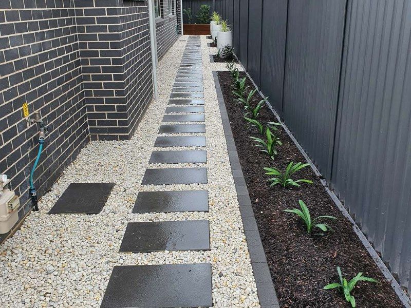 A Walkway Between A Brick Building And A Fence — Green Envy Landscape & Garden Services In Cameron Park NSW