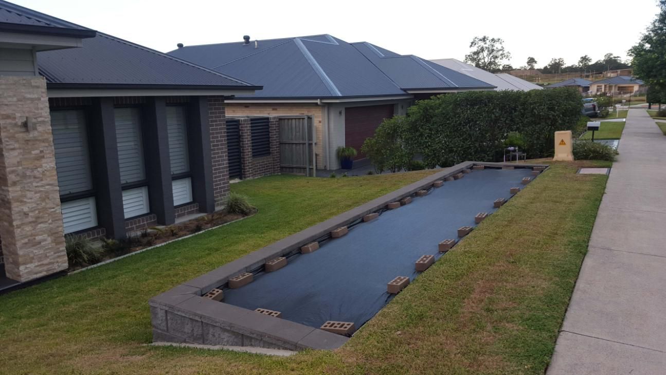 A Long, Rectangular Pool Covered in Dark Fabric Sits — Green Envy Landscape & Garden Services In Cameron Park NSW
