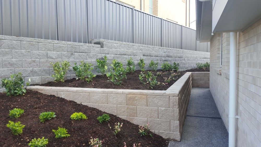 A Brick Wall With A Planter In The Middle Of It Next To A House — Green Envy Landscape & Garden Services In Cameron Park NSW