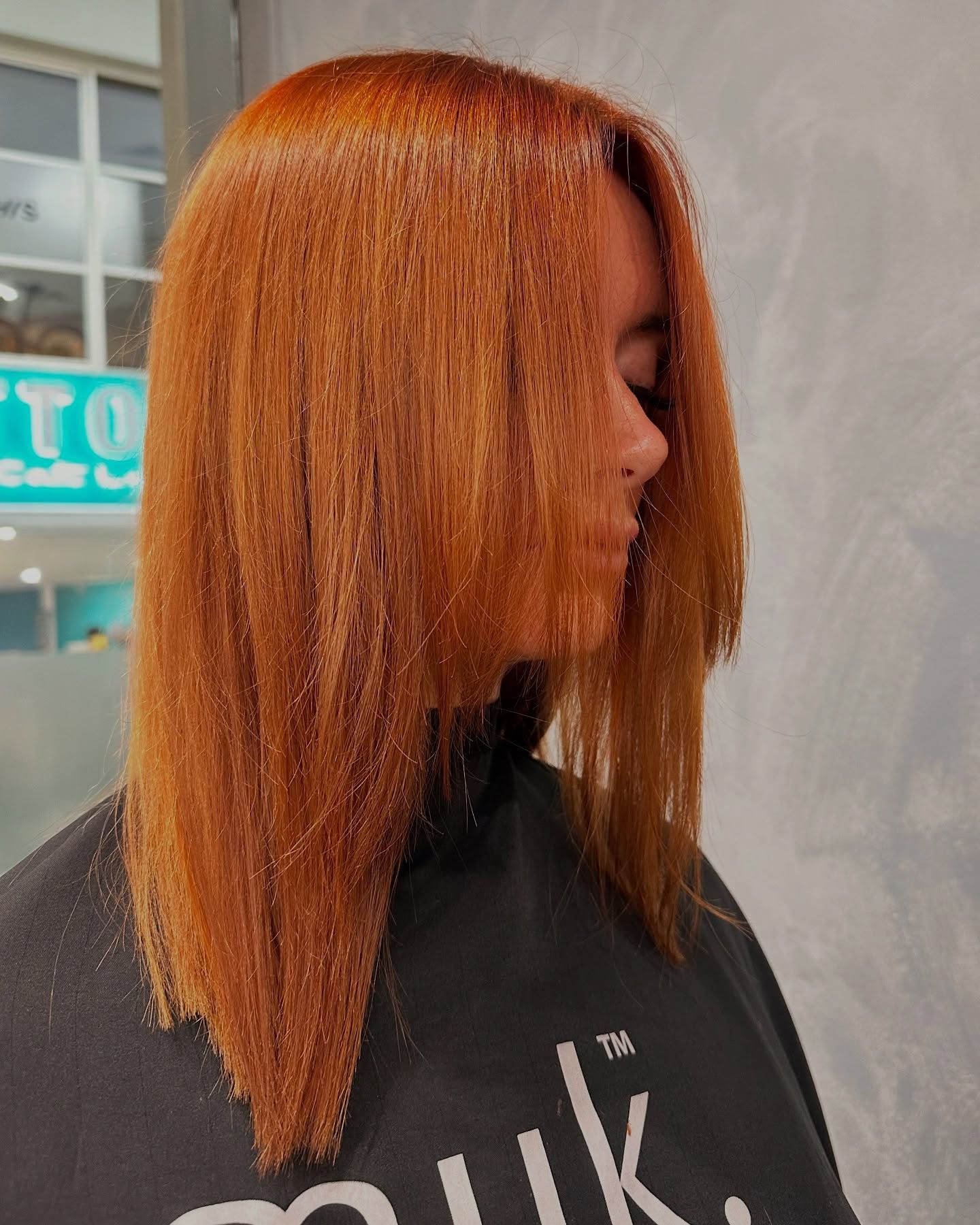 A Woman With Long orange Hair is Standing in a Salon — AW Hair Studios - Surfers Paradise in Surfers Paradise, QLD