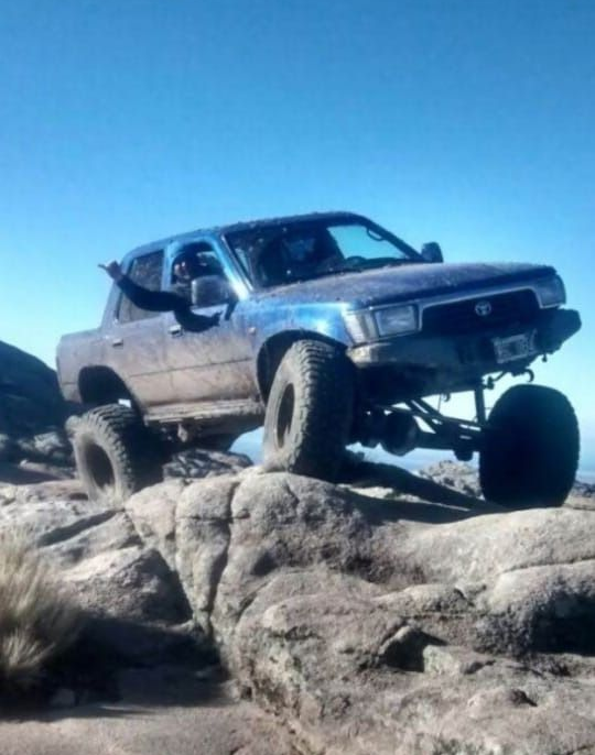 Camión todoterreno Toyota azul subiendo un terreno rocoso bajo un cielo azul claro.
