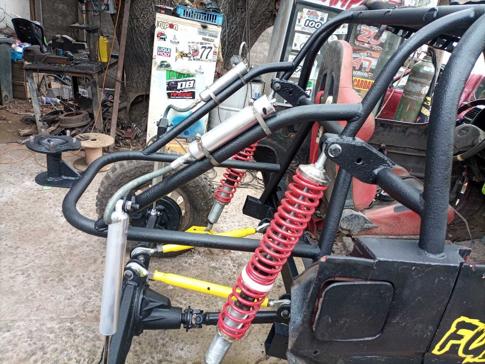 Chasis de buggy negro con amortiguadores rojos y brazos de suspensión amarillos, en taller.