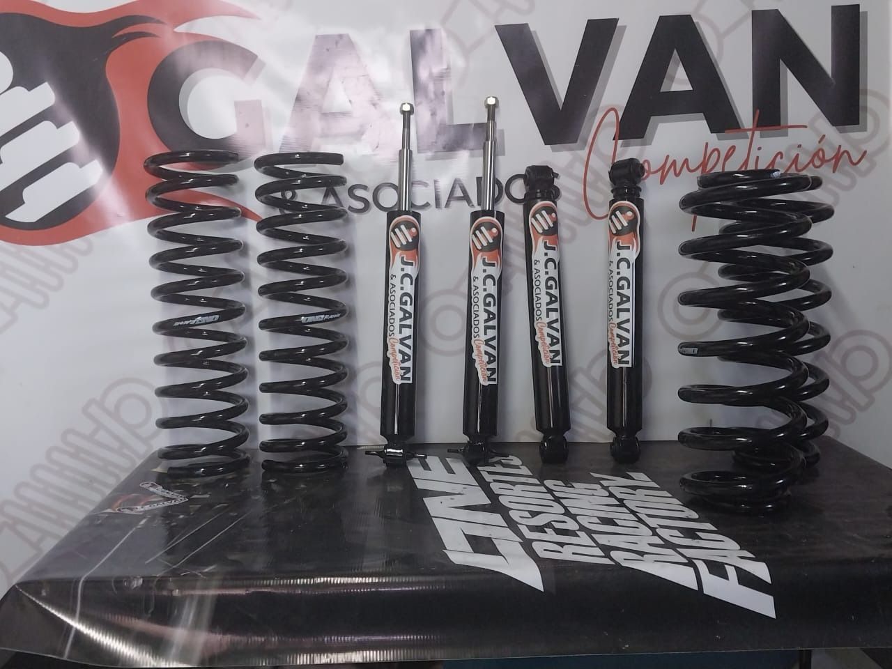 Kit de suspensión con muelles y amortiguadores de color negro expuestos delante de un logotipo.