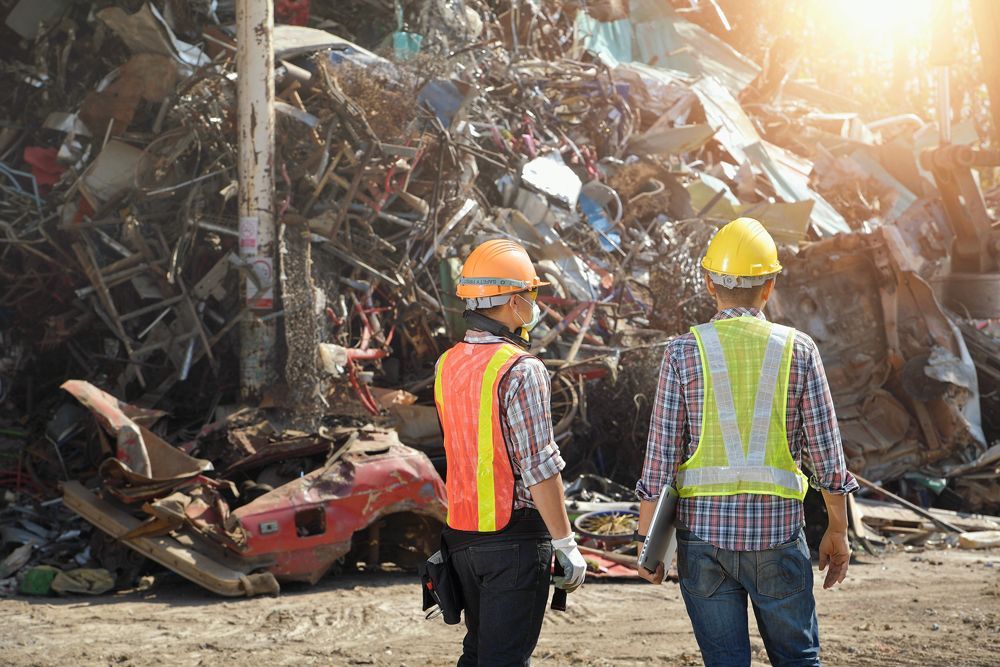 Two construction workers are standing in front of a pile of scrap metal.