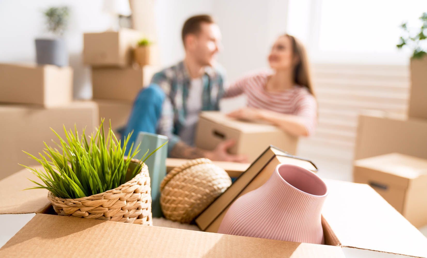A man and a woman are sitting in a living room surrounded by cardboard boxes.