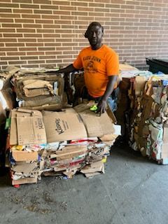 A man in an orange shirt is standing next to a pile of cardboard boxes.