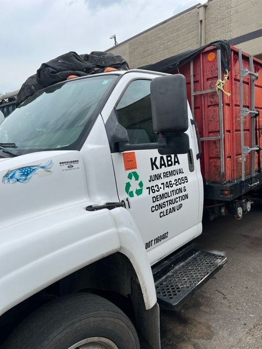 A white garbage truck is parked in front of a building.