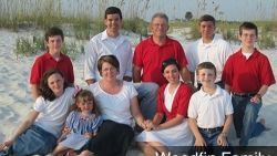 A large family is posing for a picture on the beach.